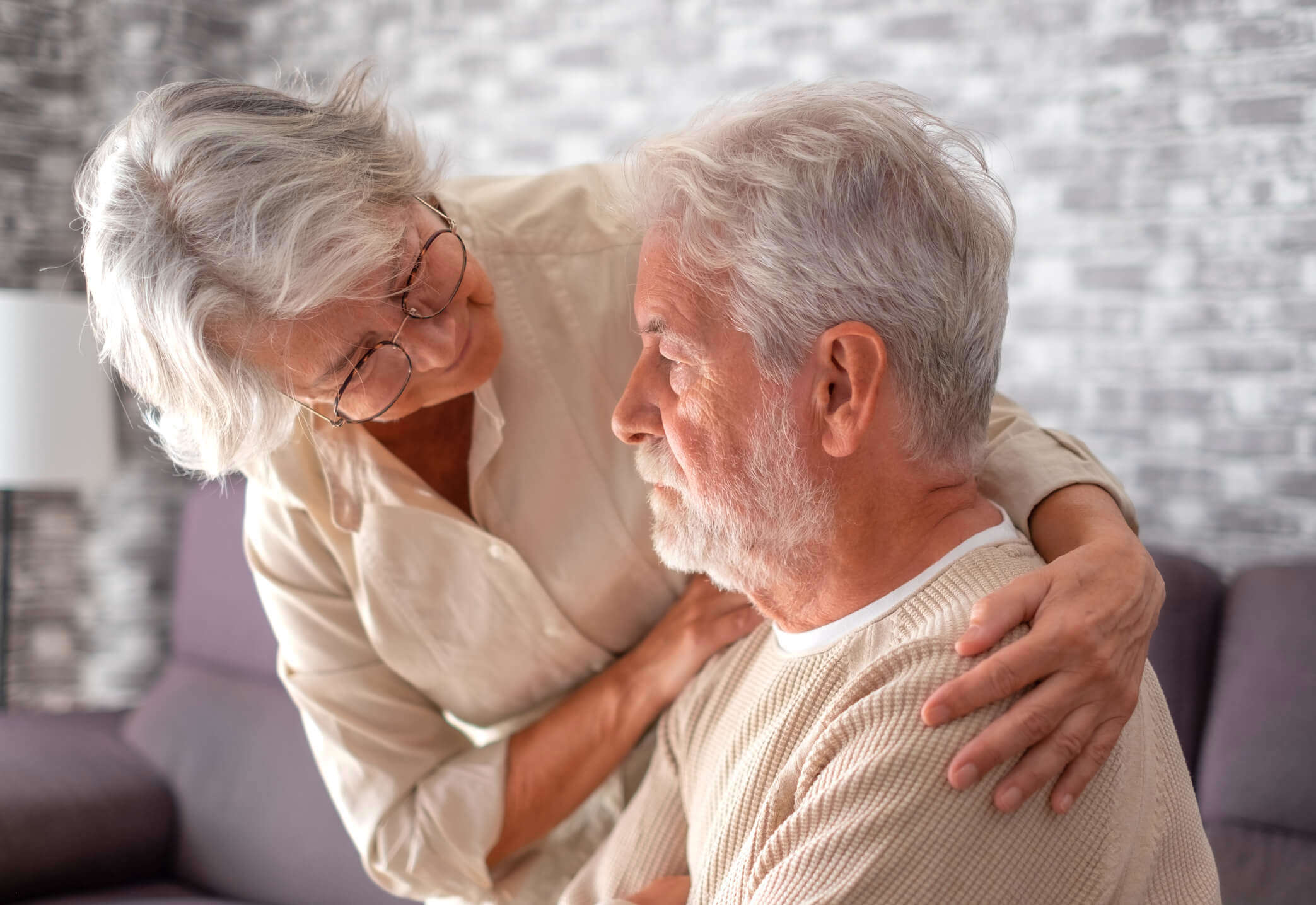 An older woman comforting an older man with her arms around his shoulders