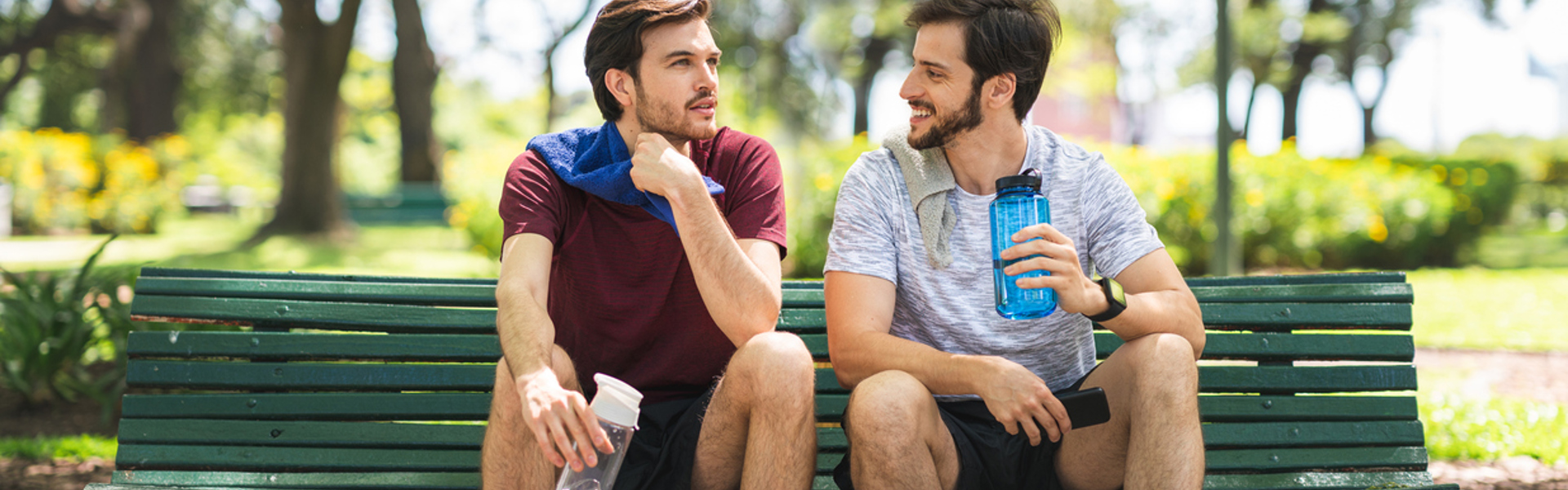 two men sat on a park bench talking after doing some exercise