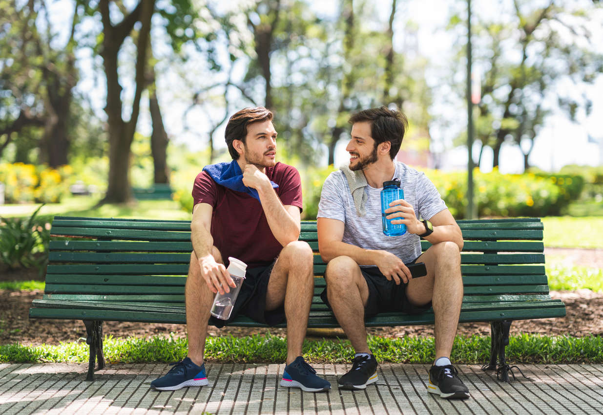 two men sat on a park bench talking after doing some exercise