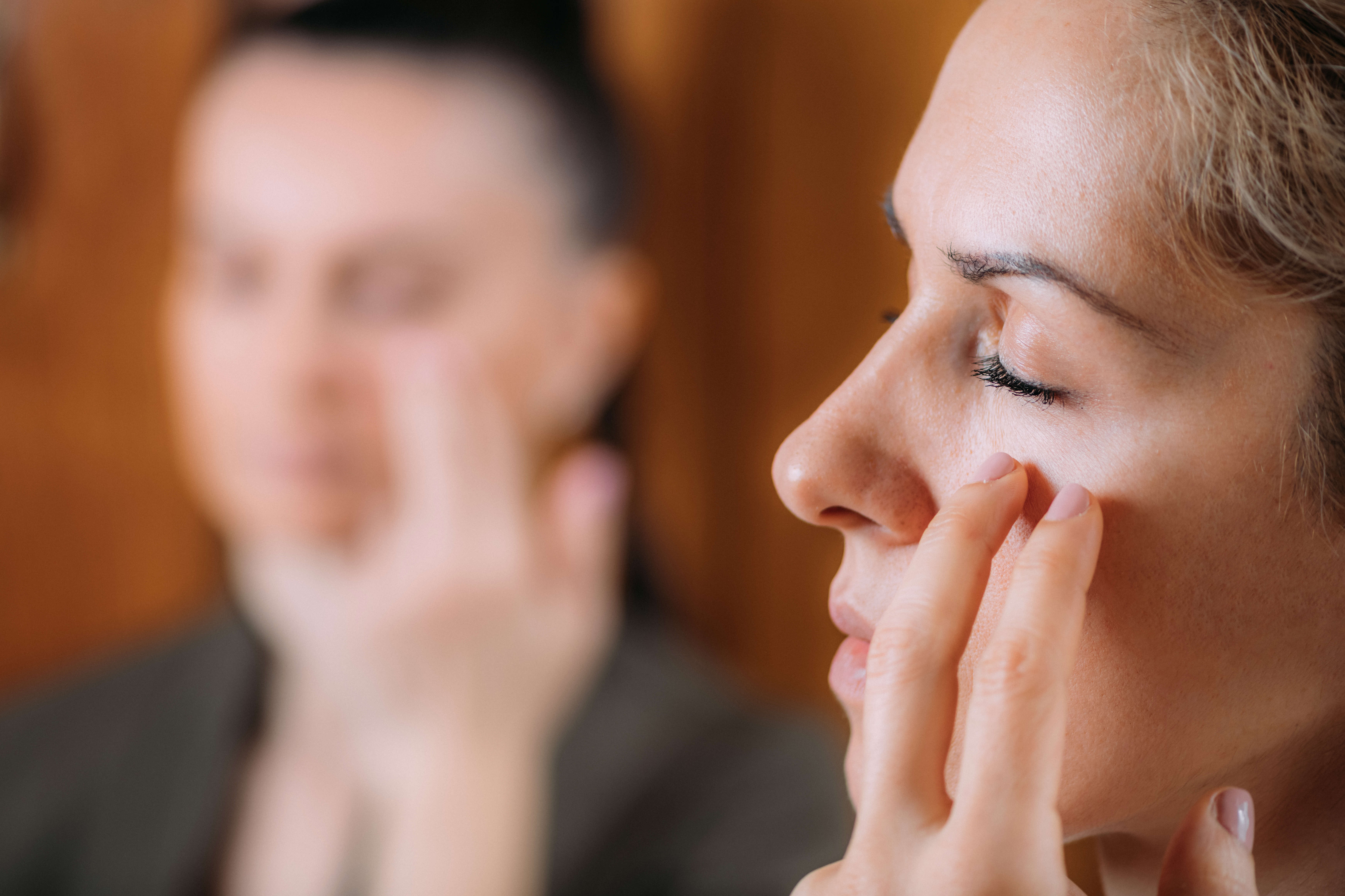 Main Image: a woman practicing EFT tapping, tapping on her face with her eyes shut.