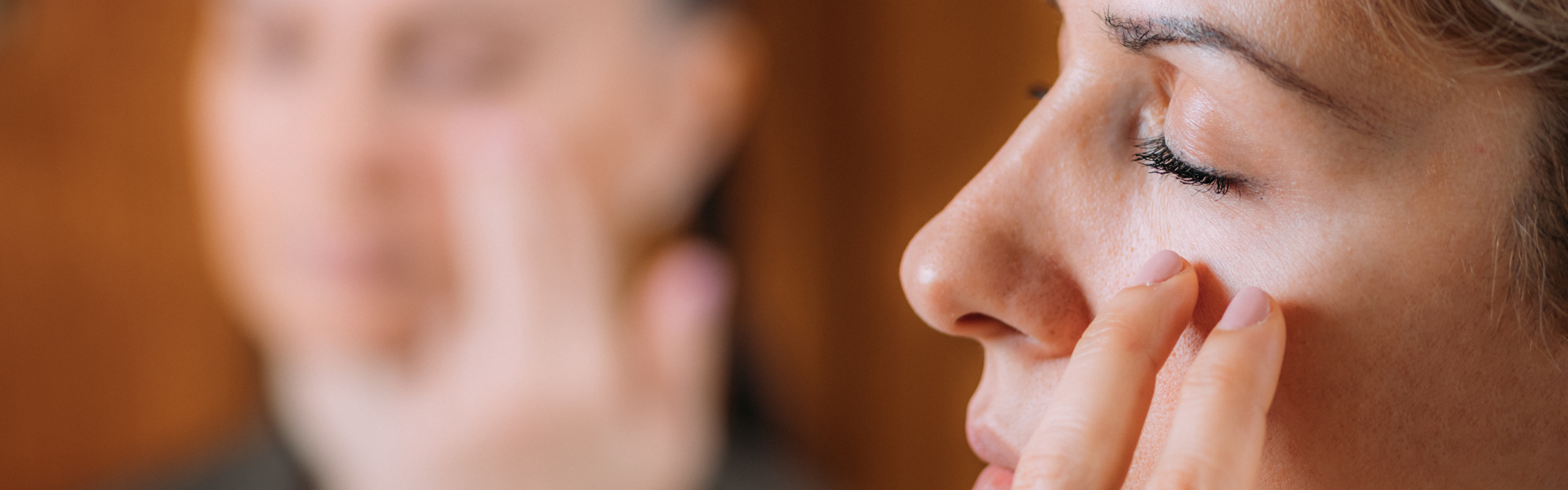 Main Image: a woman practicing EFT tapping, tapping on her face with her eyes shut.