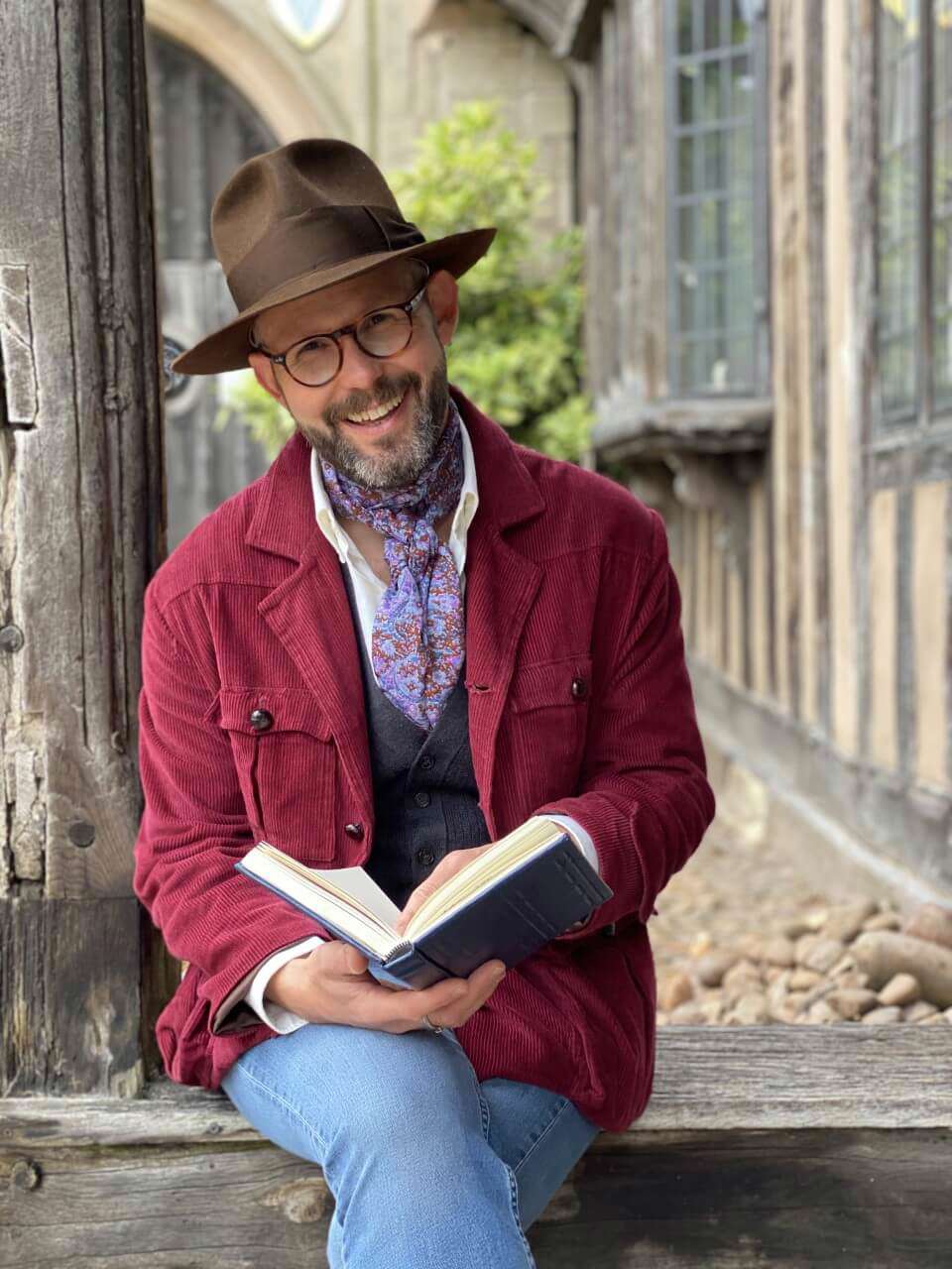 Crafter Mark Francis sat on a wall wearing a fedora hat with an open book on his lap