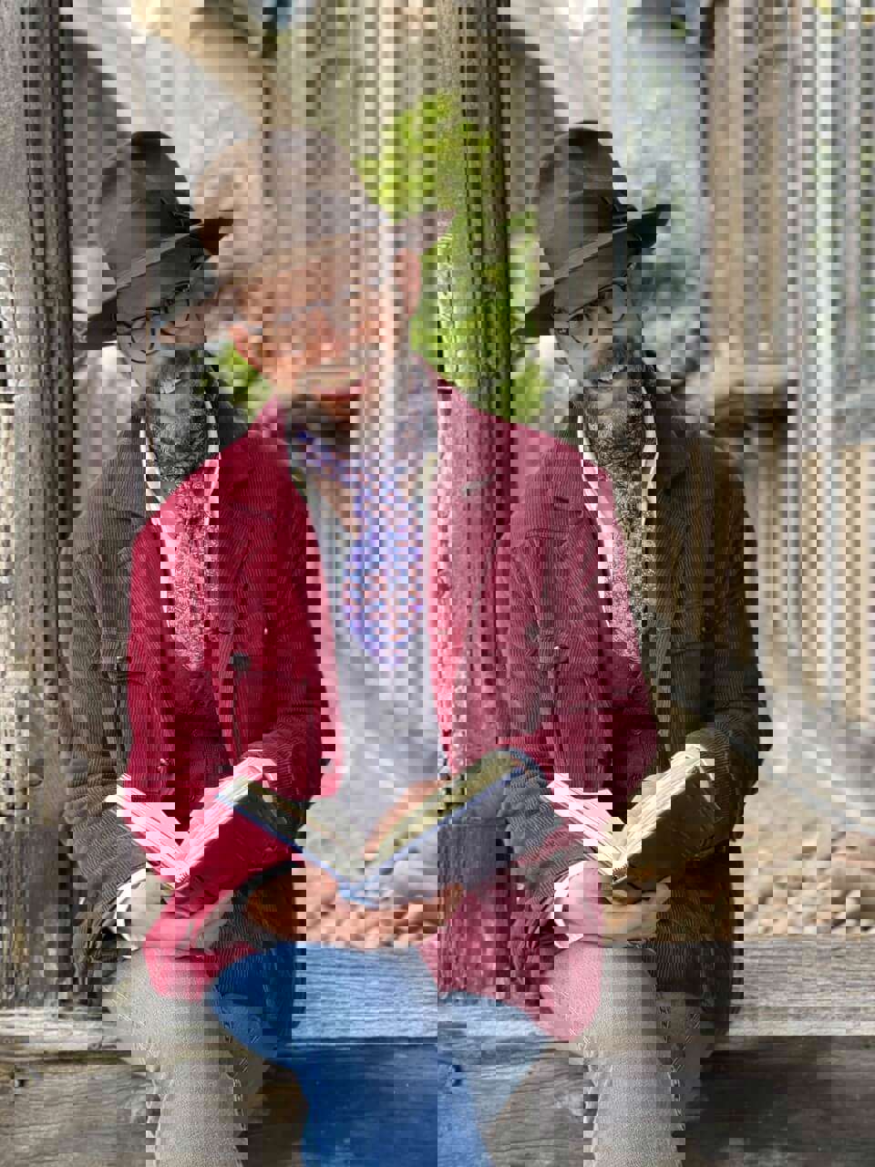 Crafter Mark Francis sat on a wall wearing a fedora hat with an open book on his lap