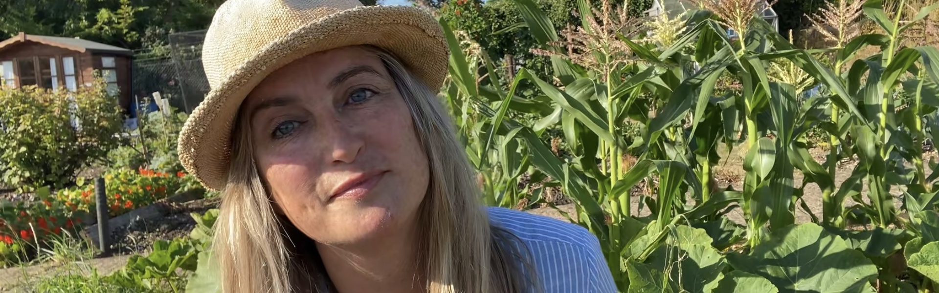 landscape photo of rachel moore wearing a hat in front of her allotment on a bright sunny day