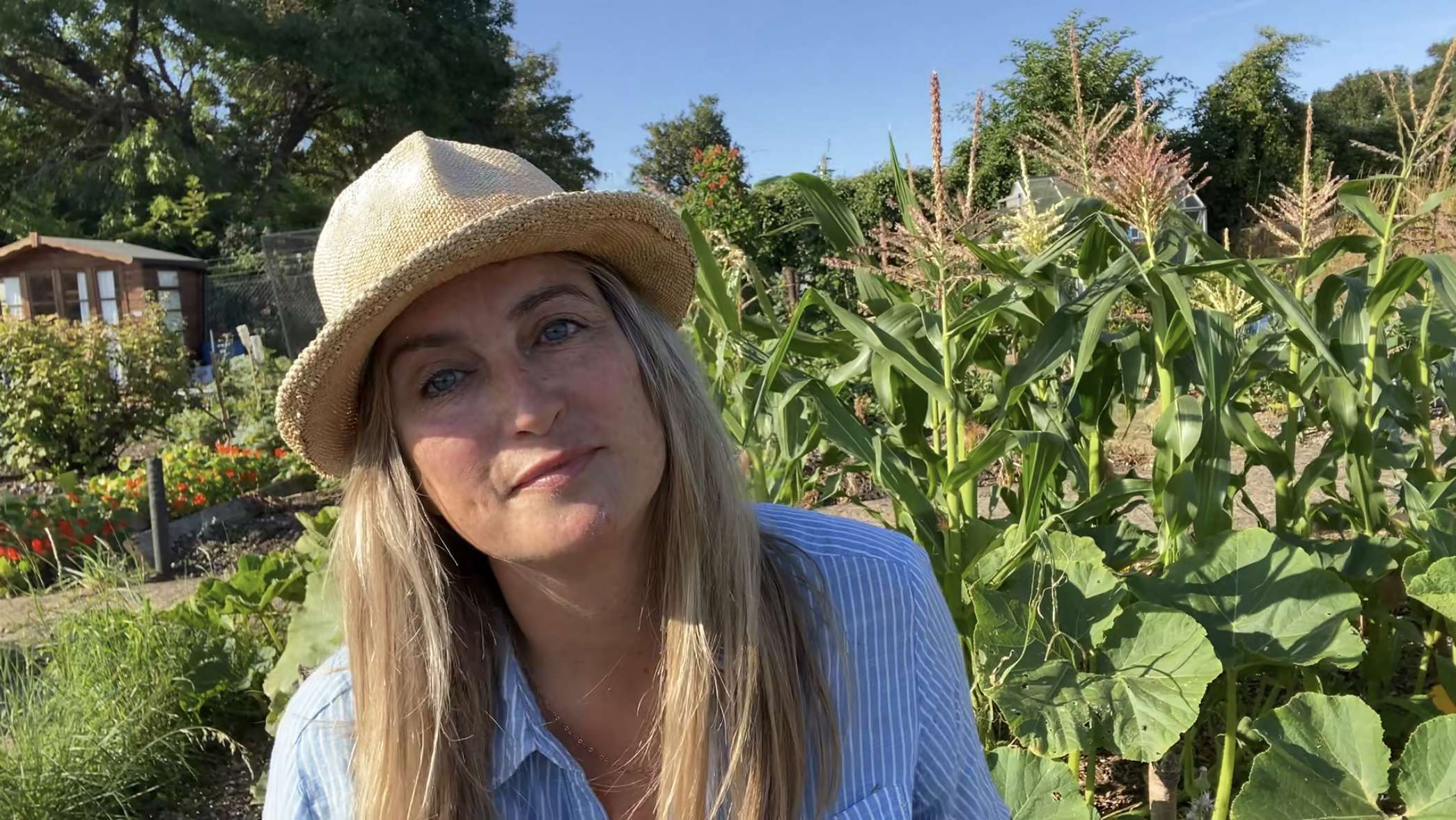 landscape photo of rachel moore wearing a hat in front of her allotment on a bright sunny day