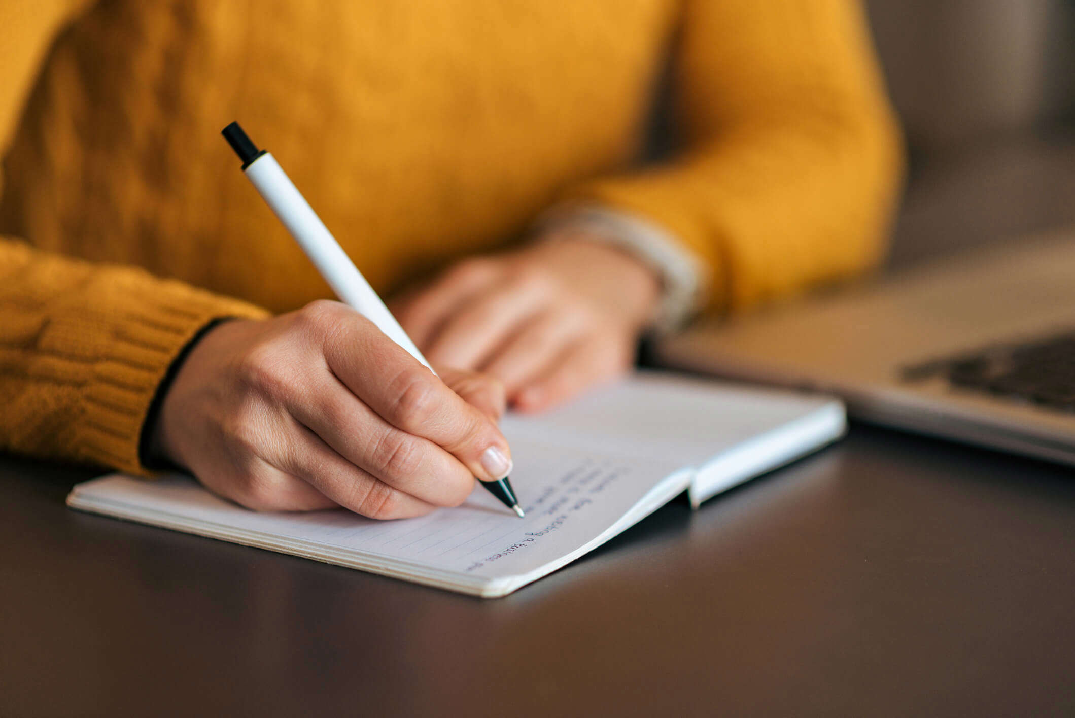 a close up of someone wearing a yellow jumper writing in a journal