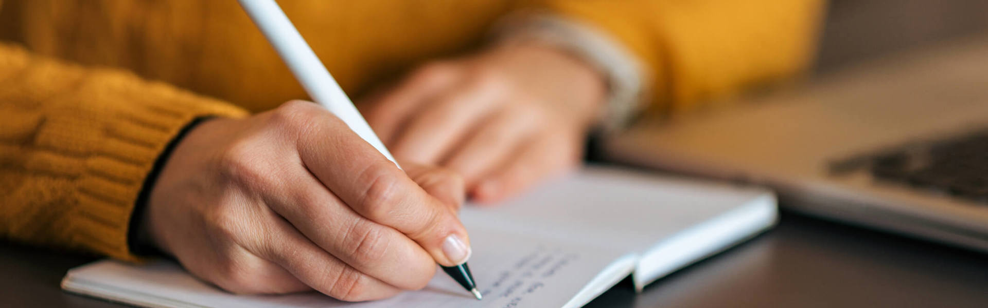 a close up of someone wearing a yellow jumper writing in a journal