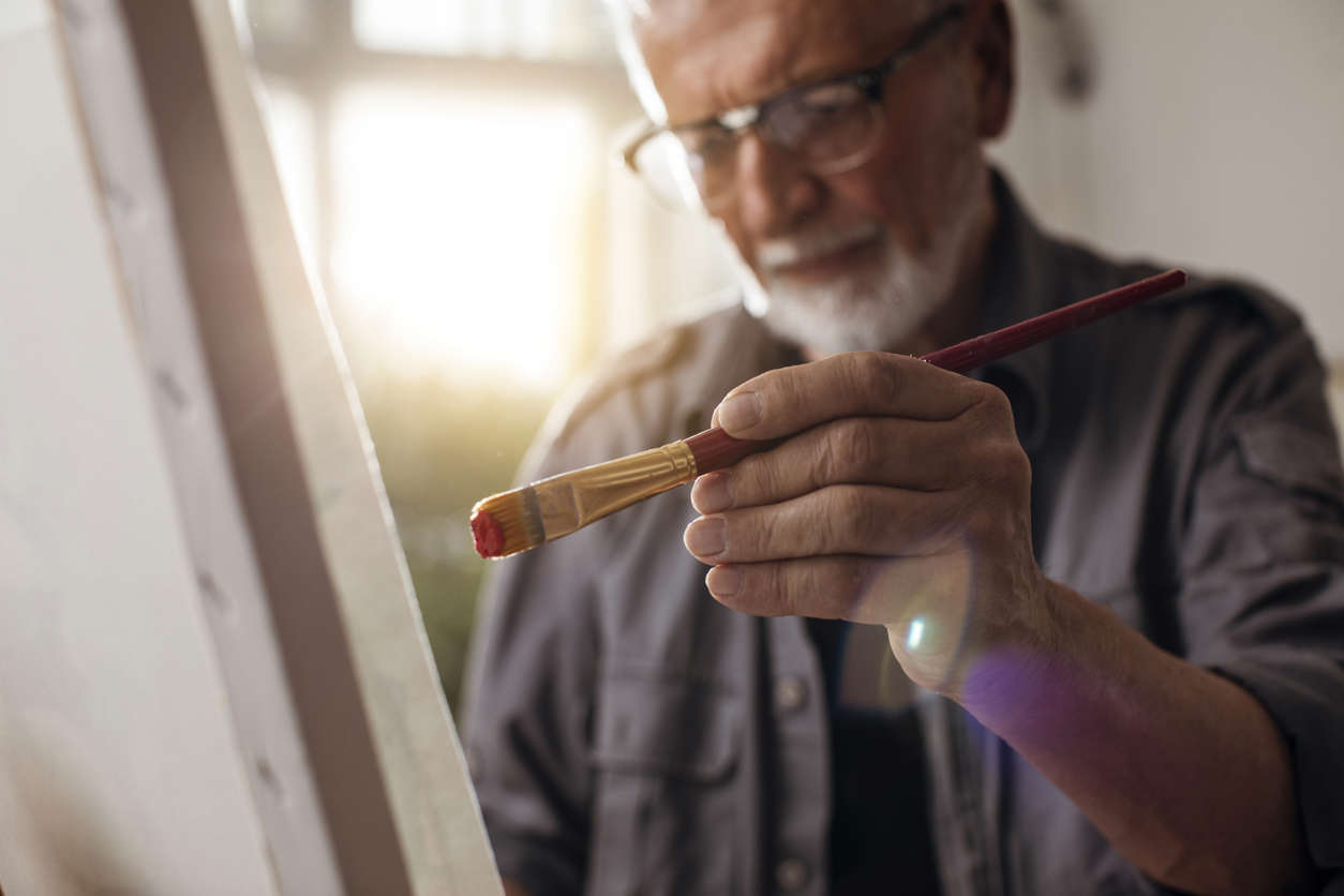 elderly male holding a paintbrush with his left hand painting on canvas