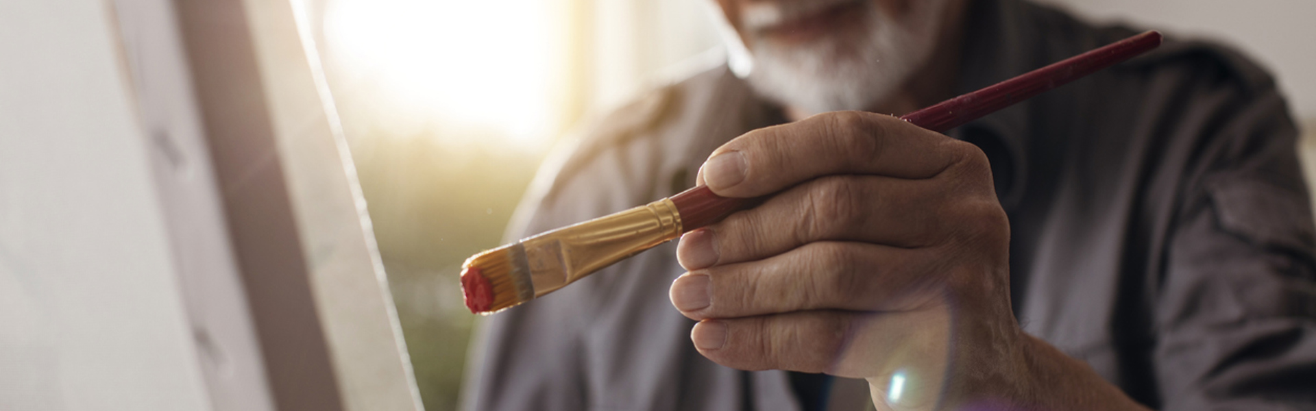 elderly male holding a paintbrush with his left hand painting on canvas