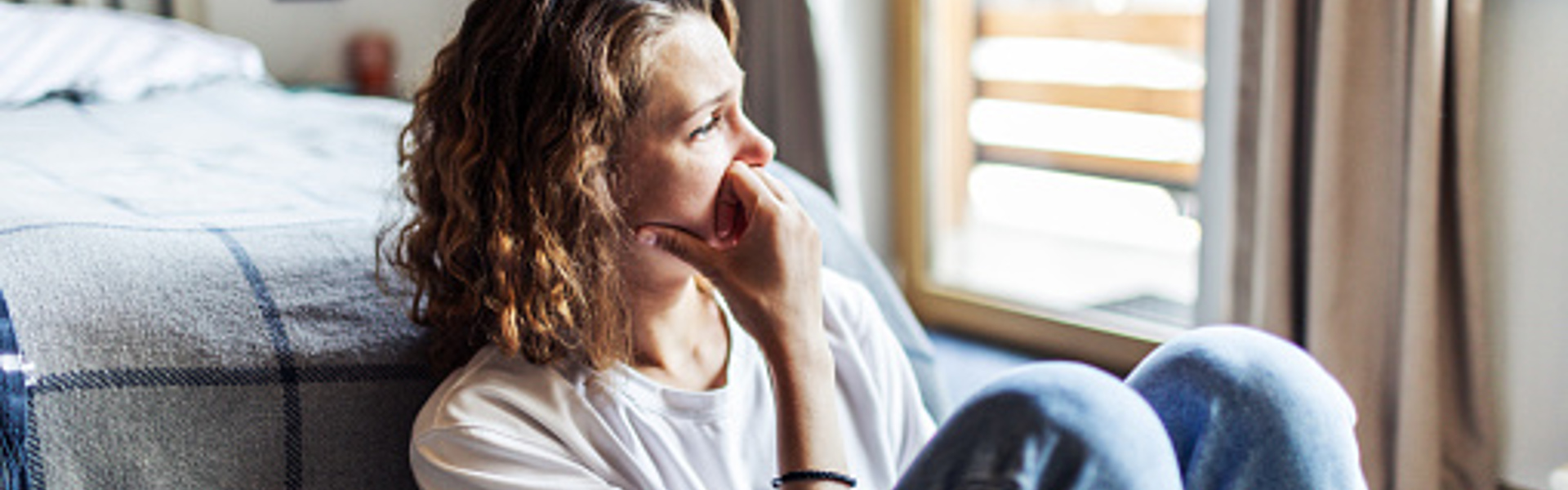 a woman sat at the end of her bed looking sad