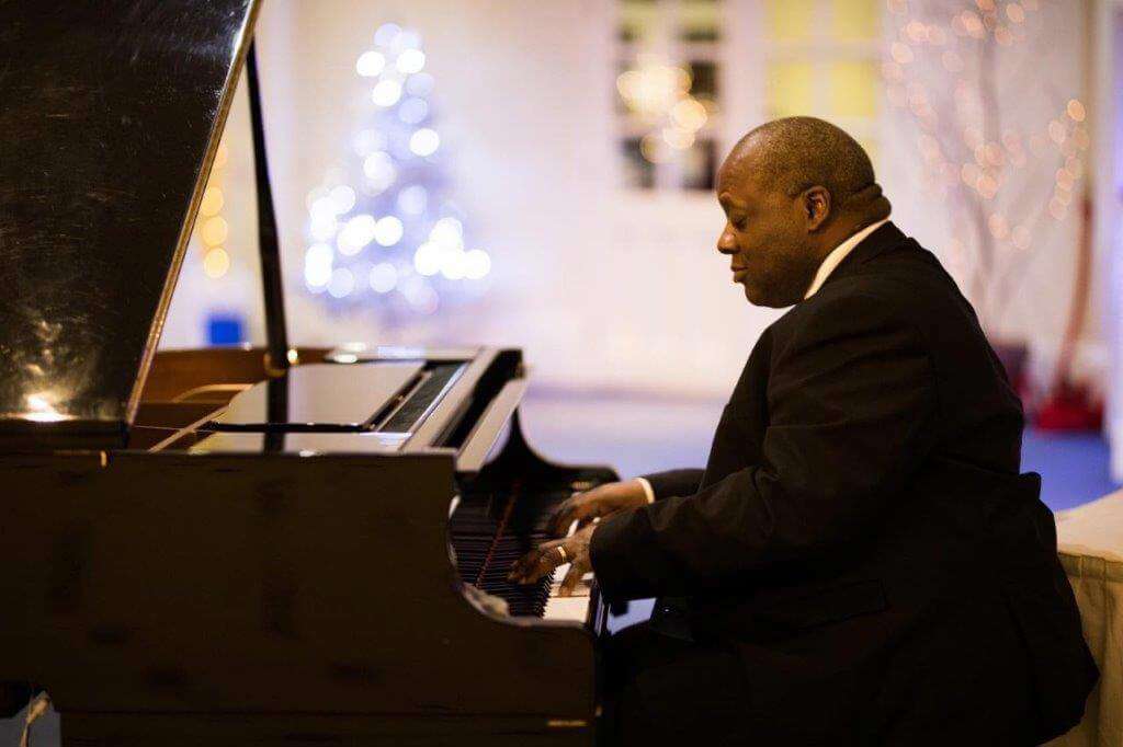 Pianist Lincoln Noel sat at a black grand piano with Christmas lights in the background