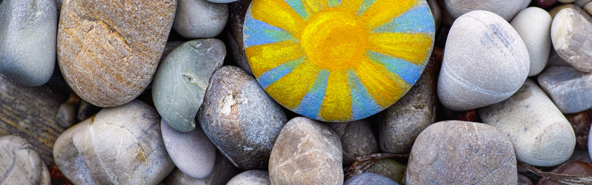 a close up of beach pebbles with one painted blue and yellow in the pattern of a sun