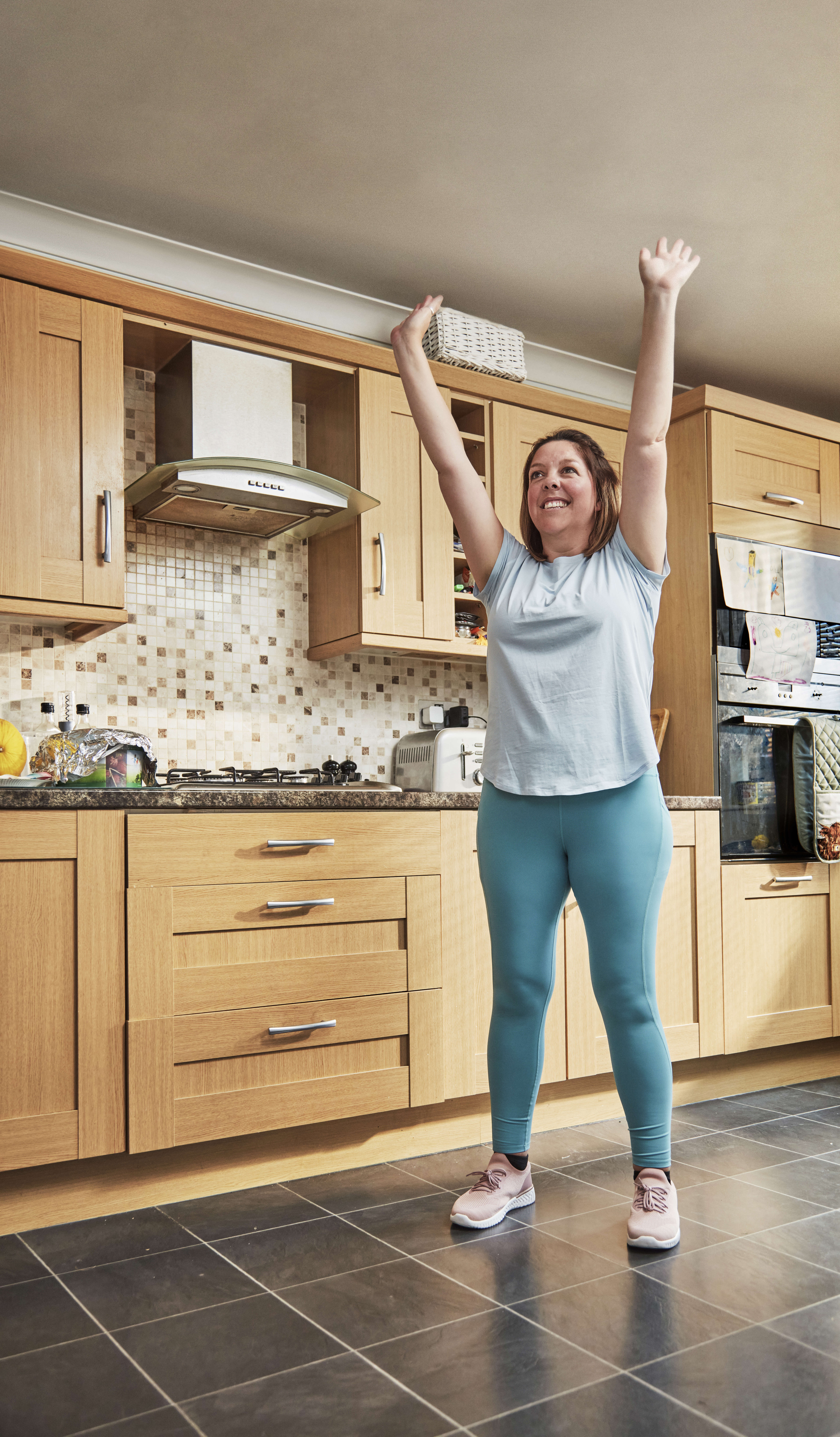 Main image: a woman stretching up to the ceiling in her kitchen, wearing exercise clothing. Taking part in balance exercises for fall prevention.