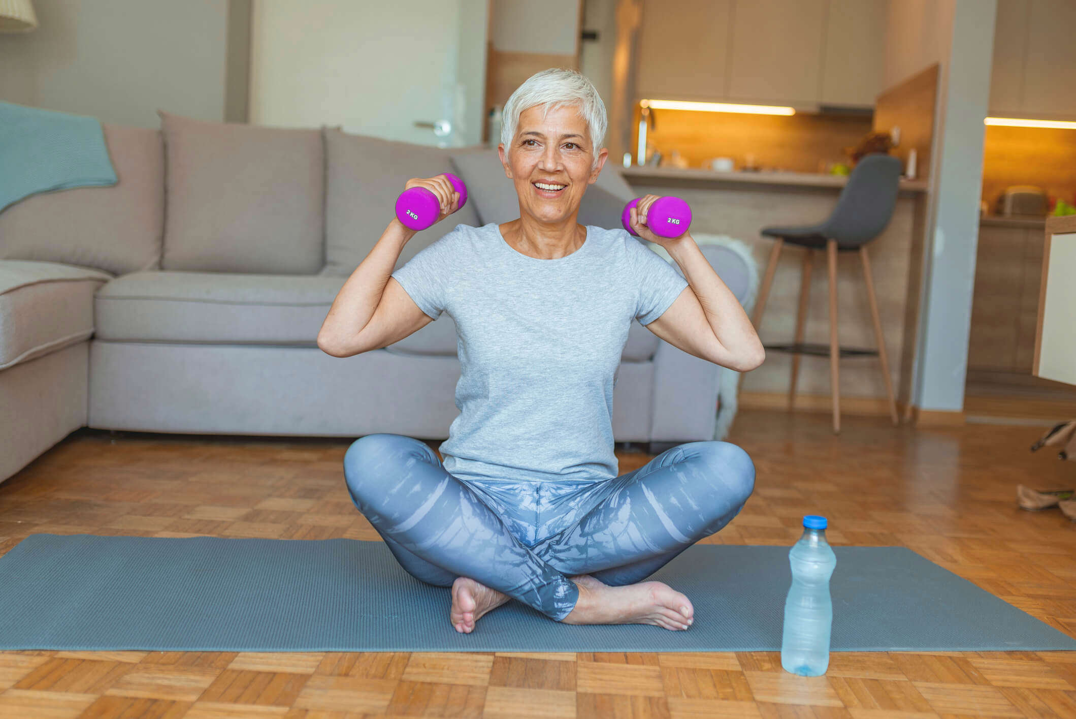 a woman with white grey hair sat cross legged on the floor holding purple hand weights