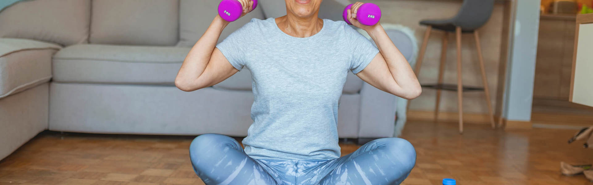 a woman with white grey hair sat cross legged on the floor holding purple hand weights