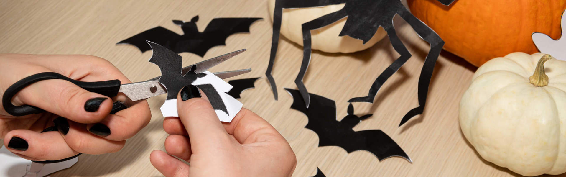 someone cutting halloween bats and spiders out of black card with an orange pumpkin in the background