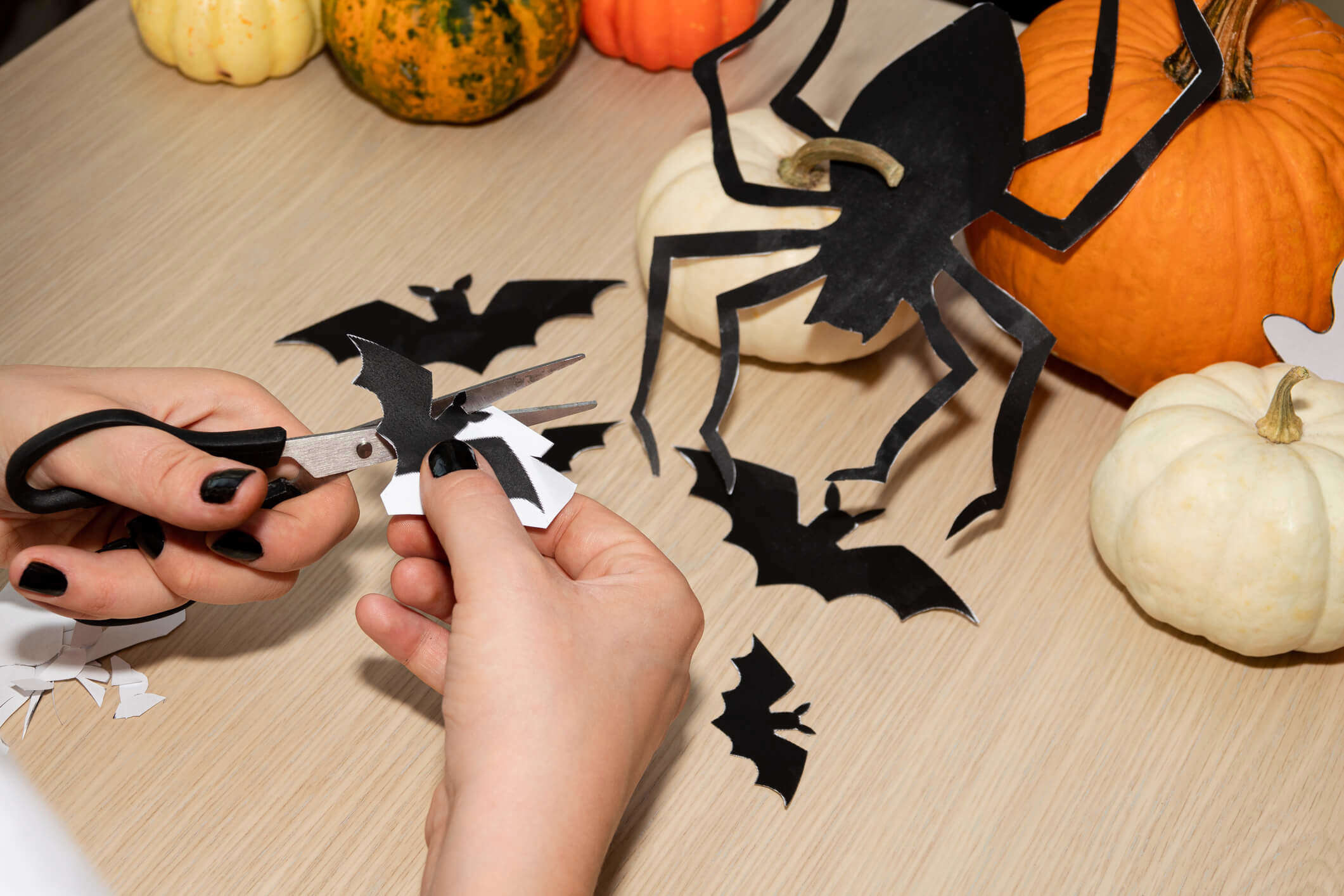 someone cutting halloween bats and spiders out of black card with an orange pumpkin in the background