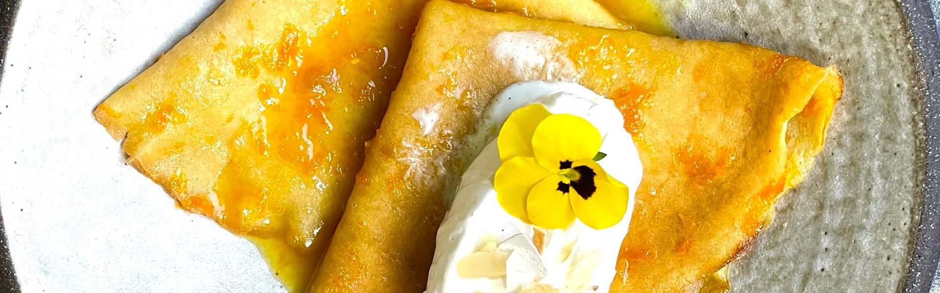 fresh homemade Crepes Suzette on a plate decorated with a scoop of white vanilla ice cream, maple syrup and a small yellow flower