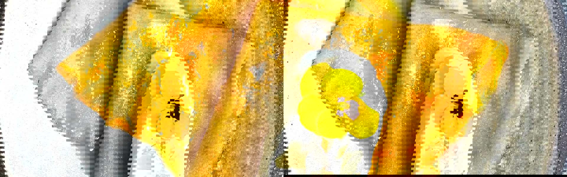 fresh homemade Crepes Suzette on a plate decorated with a scoop of white vanilla ice cream, maple syrup and a small yellow flower