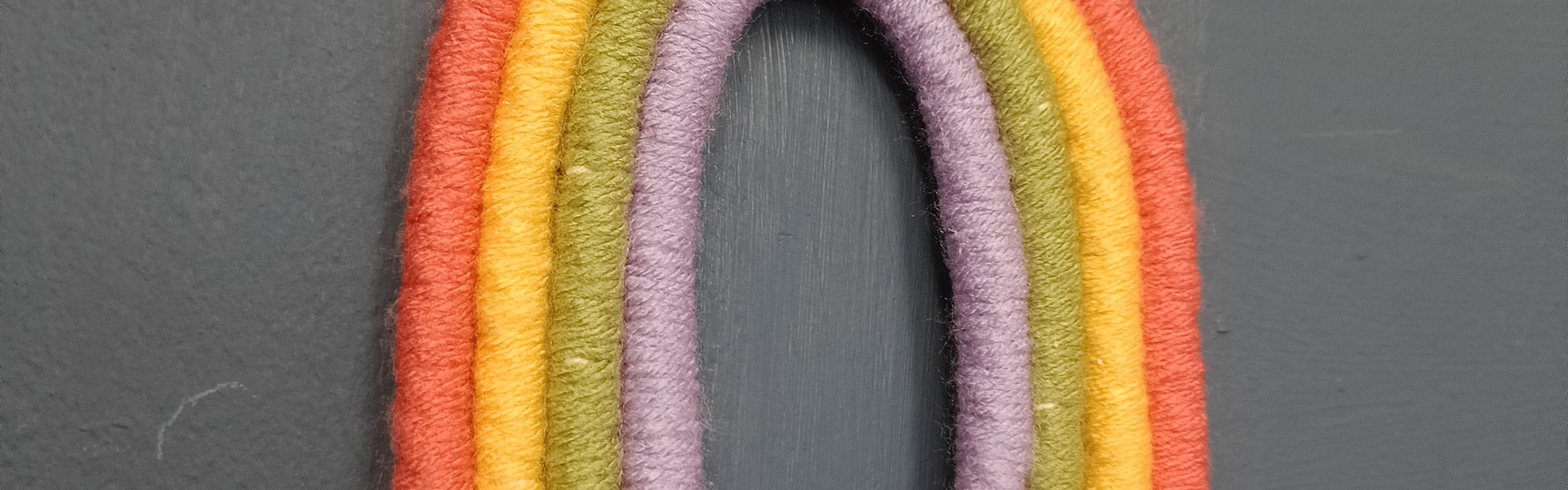 Wall hanging of a rainbow made from rope in the four colours from the inside out of purple, green, yellow and orange