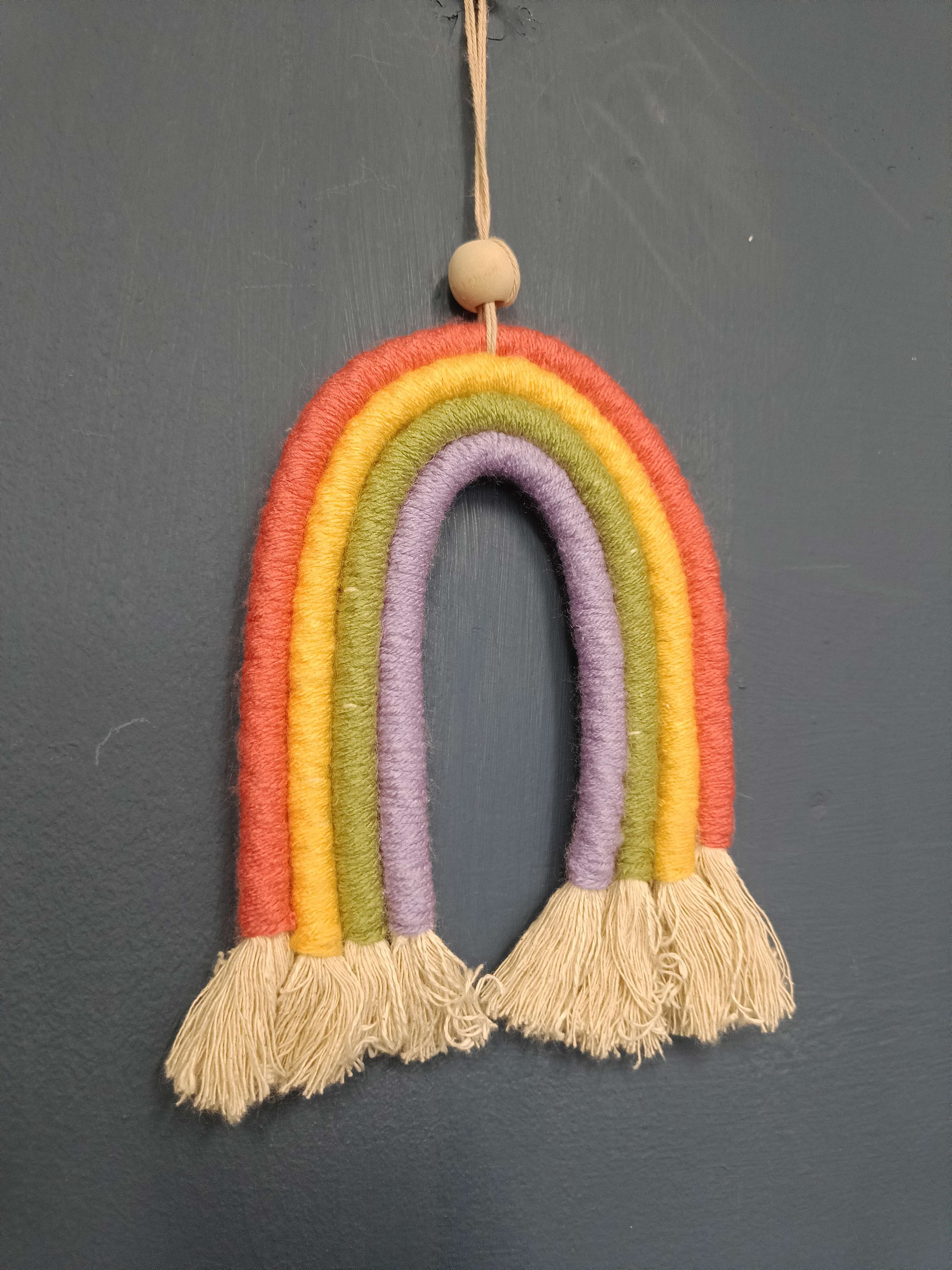 Wall hanging of a rainbow made from rope in the four colours from the inside out of purple, green, yellow and orange