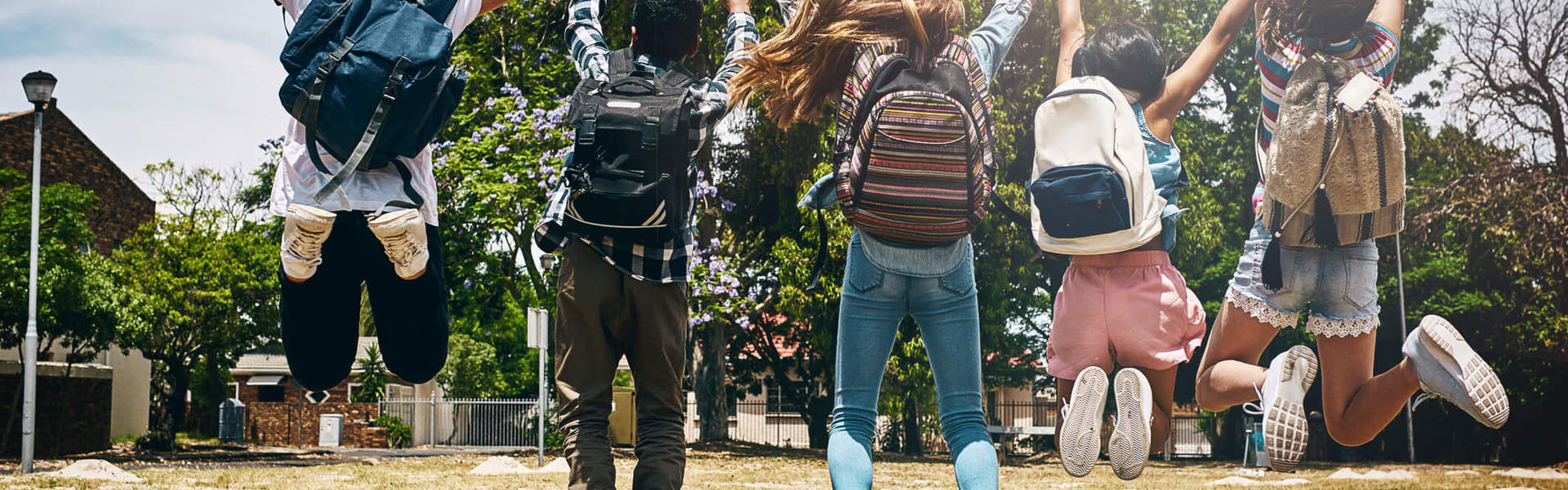 a group of school children with backpacks jumping and celebrating outside