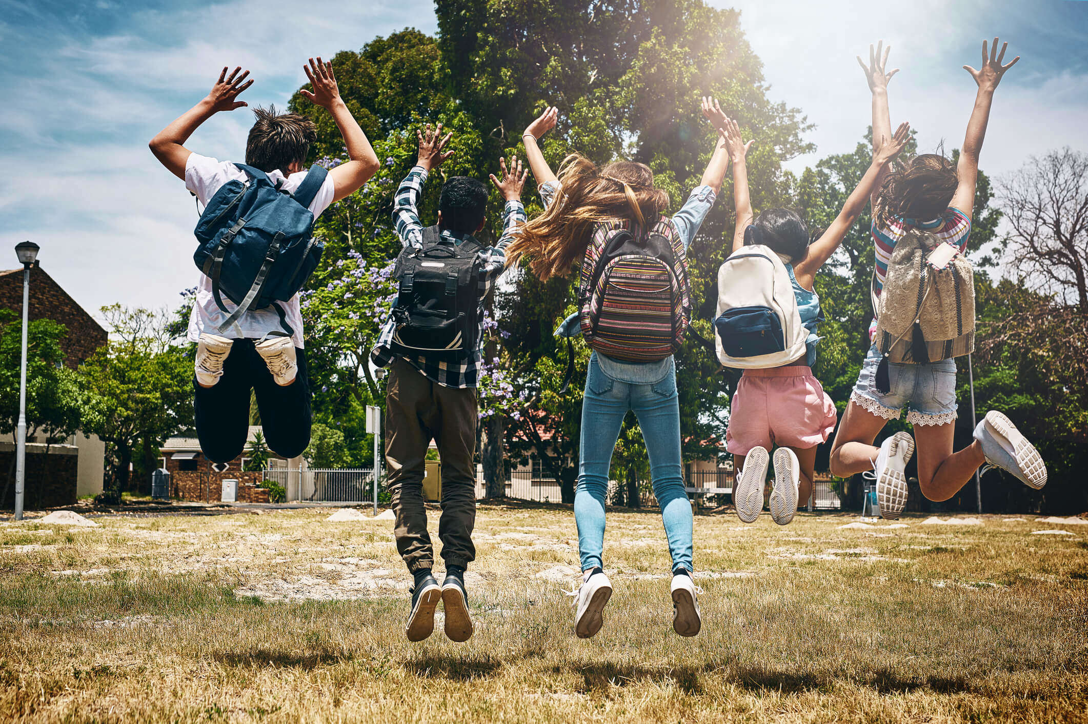 a group of school children with backpacks jumping and celebrating outside