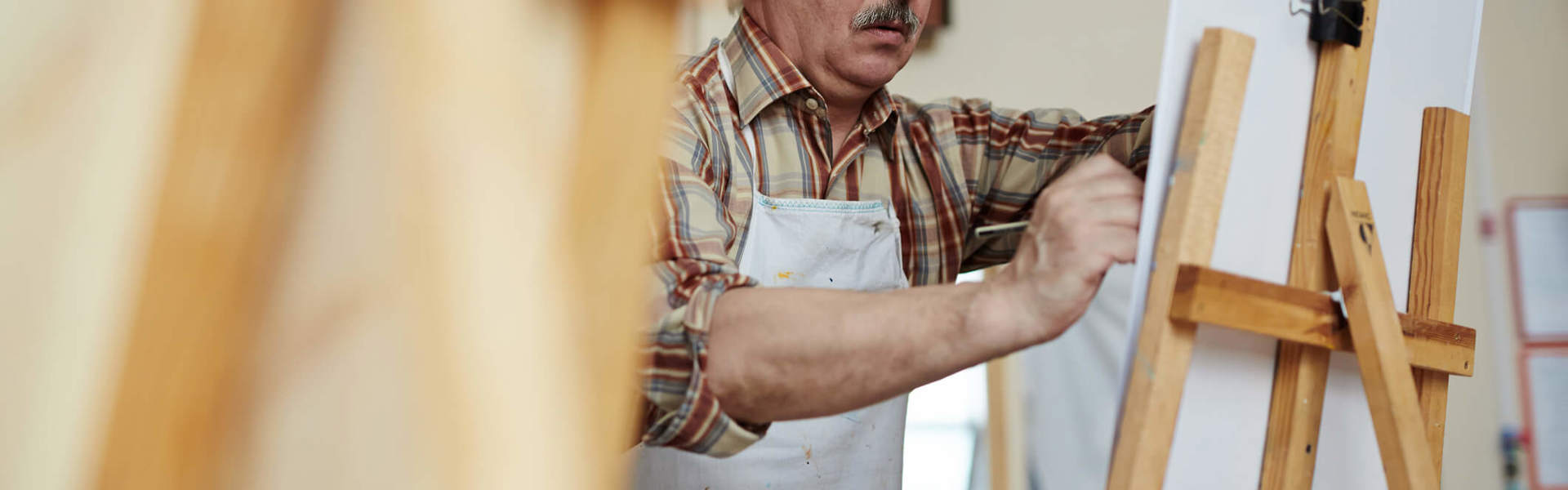 An elderly man using an easel to draw in an art class 