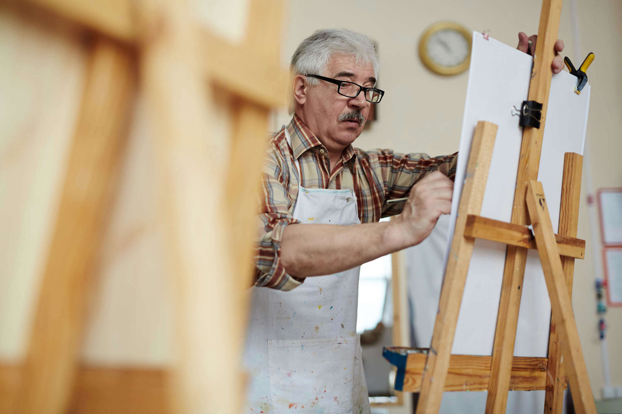 An elderly man using an easel to draw in an art class 