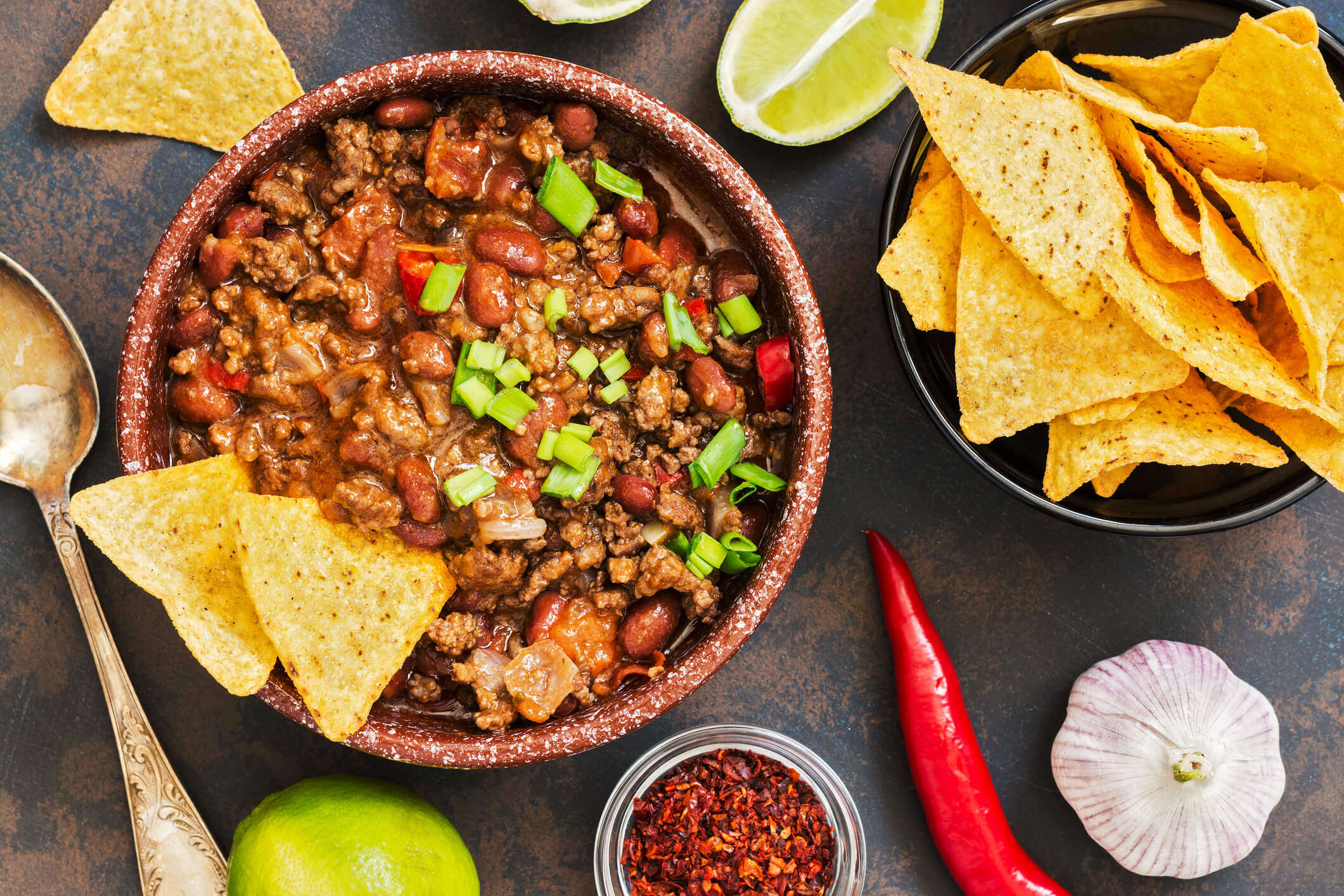 mince meat chilli with red kidney beans and green onions in a bowl with salted tortilla chips 