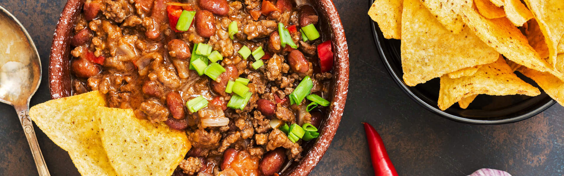 mince meat chilli with red kidney beans and green onions in a bowl with salted tortilla chips