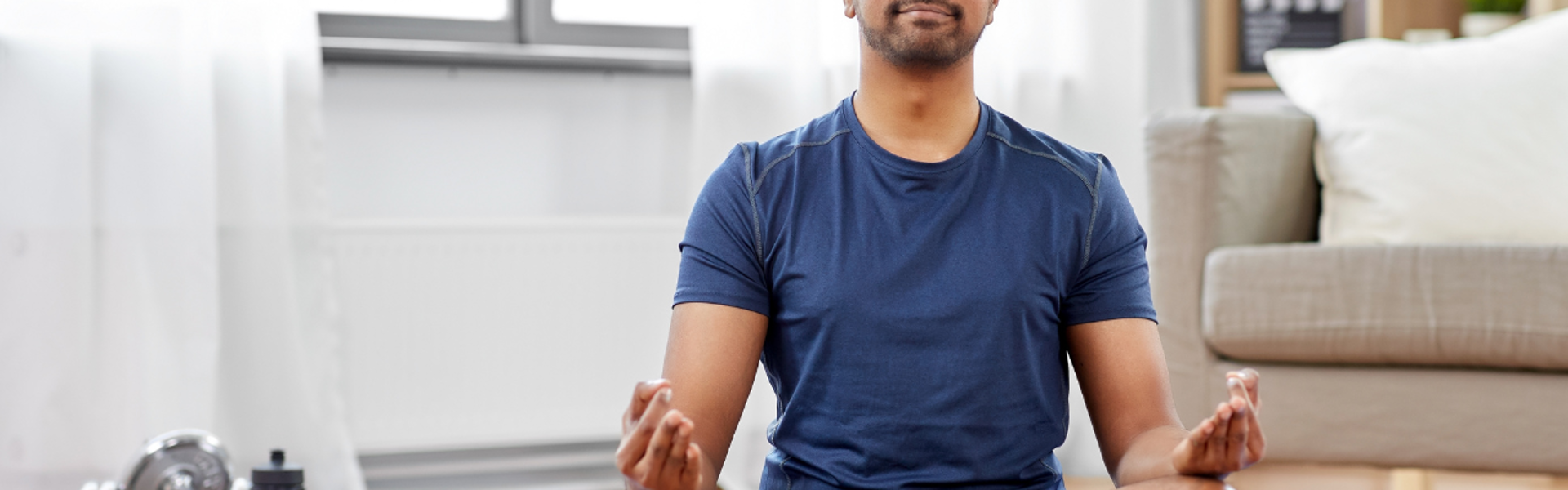 Main image: a man sat in lotus position, with eyes closed during a breathwork to calm and destress class. 