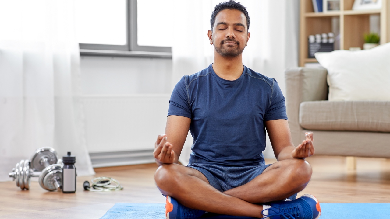 Main image: a man sat in lotus position, with eyes closed during a breathwork to calm and destress class. 