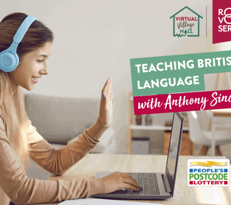 a woman wearing a camel jumper and blue over ear headphones practicing sign language using her laptop at a desk