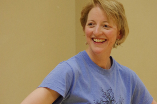 A photo of Neuro-Moves - Parkinson's Dance tutor Helen Gould MBE wearing a blue t-shirt with her hands on her hips smiling.
