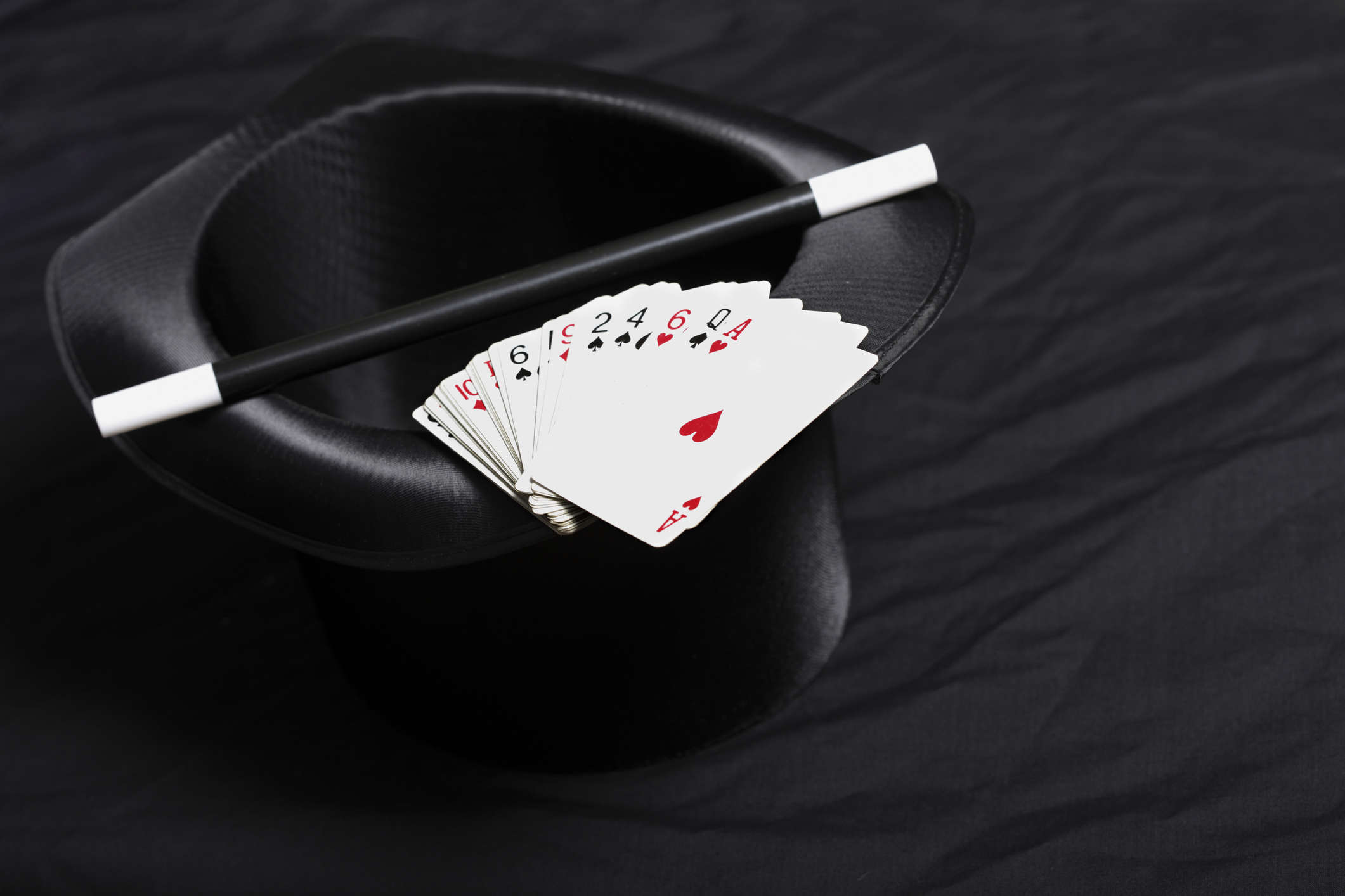Main image: a magicians black hat, with a deck of playing cards and magic wand resting on top.