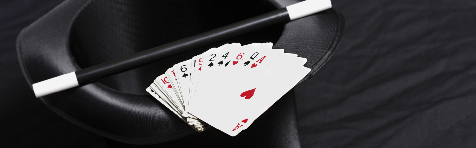 Main image: a magicians black hat, with a deck of playing cards and magic wand resting on top.