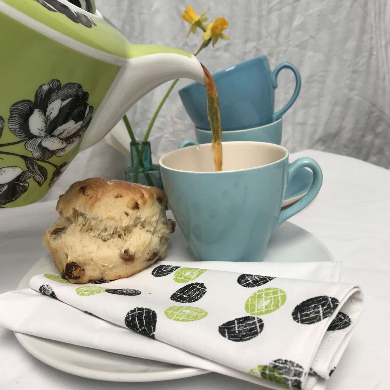 Hand printed green white and black polka dot napkin underneath a teacup and scone
