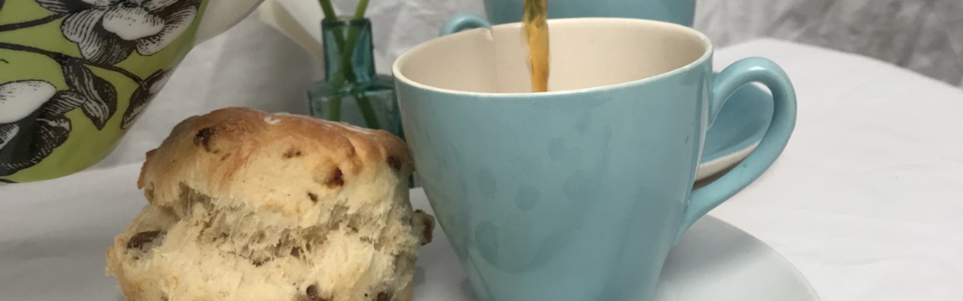 Hand printed green white and black polka dot napkin underneath a teacup and scone