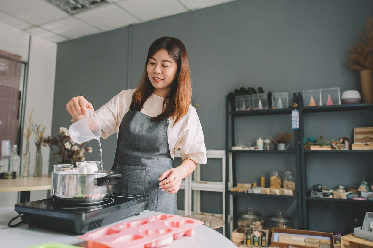 A woman wearing a pink apron making soap at home on a portable stove top