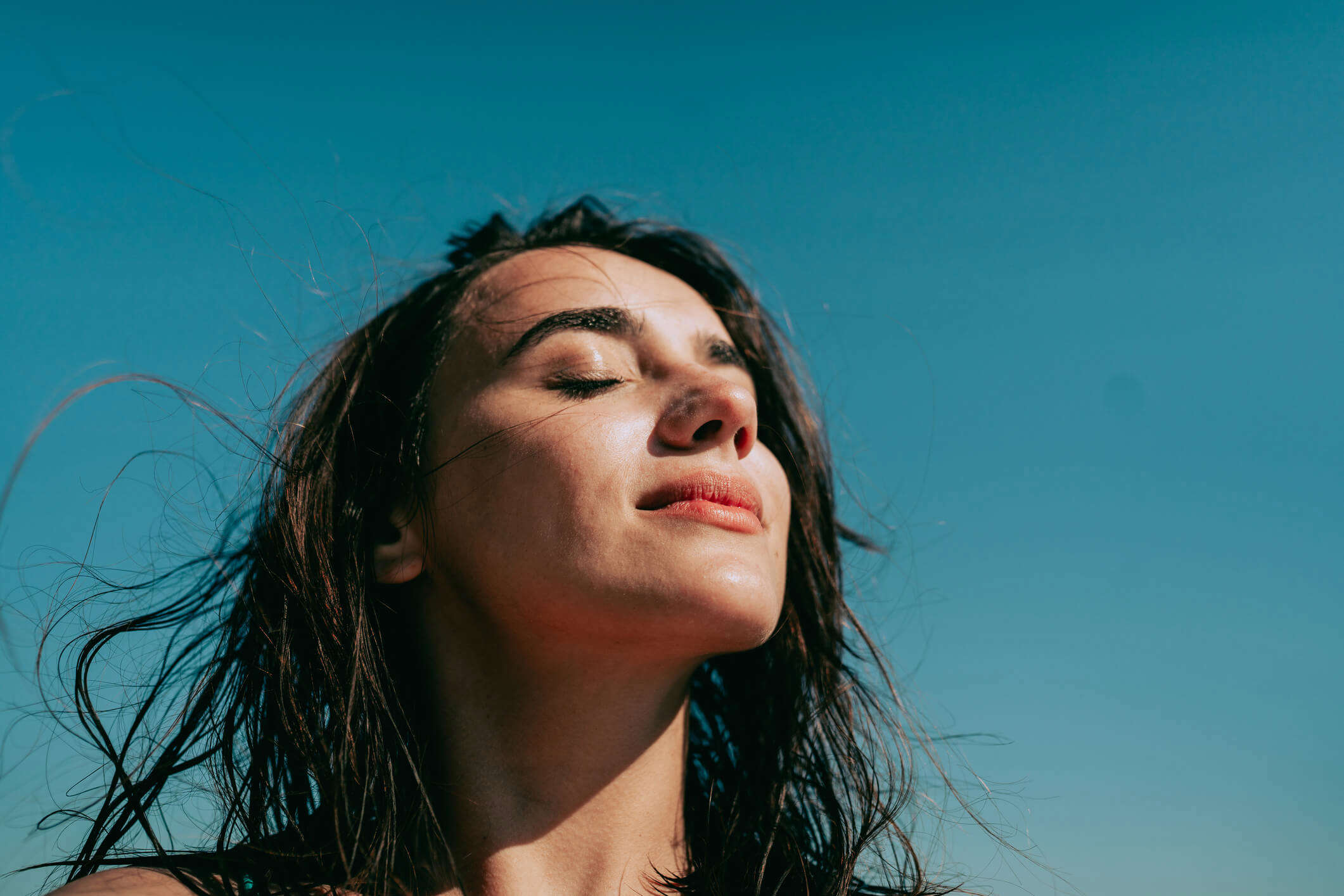 a woman with her eyes closed against a blue sky background