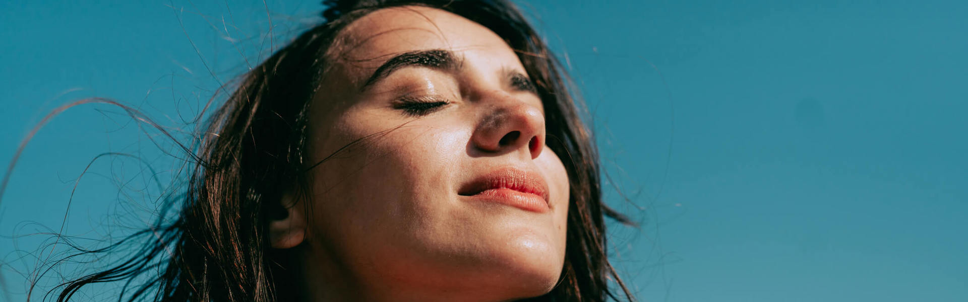 a woman with her eyes closed against a blue sky background