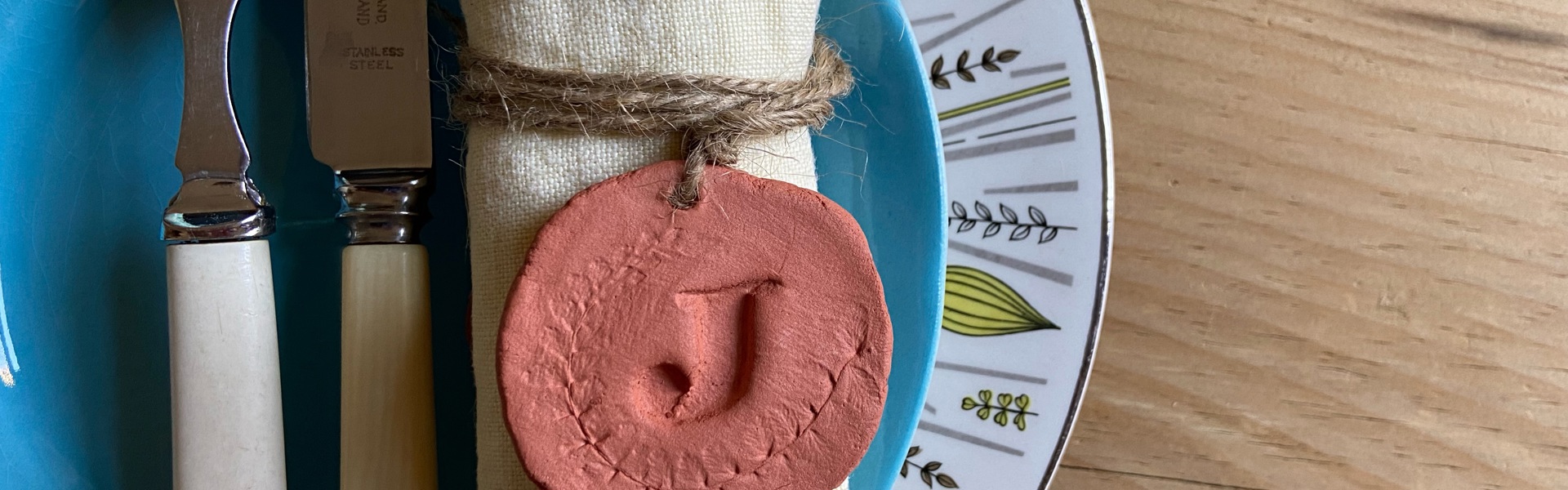 A handmade red clay monogrammed napkin holder on a dinner plate