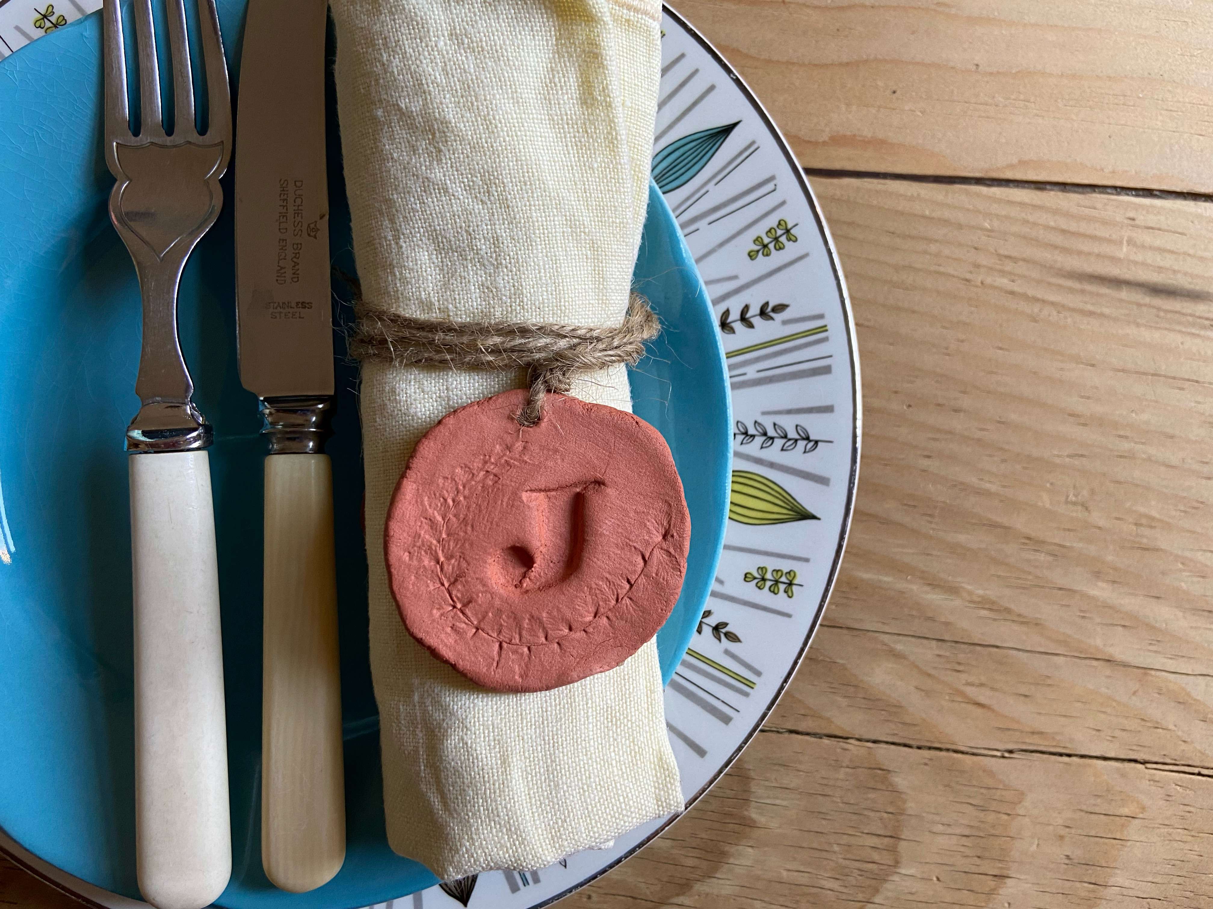 A handmade red clay monogrammed napkin holder on a dinner plate