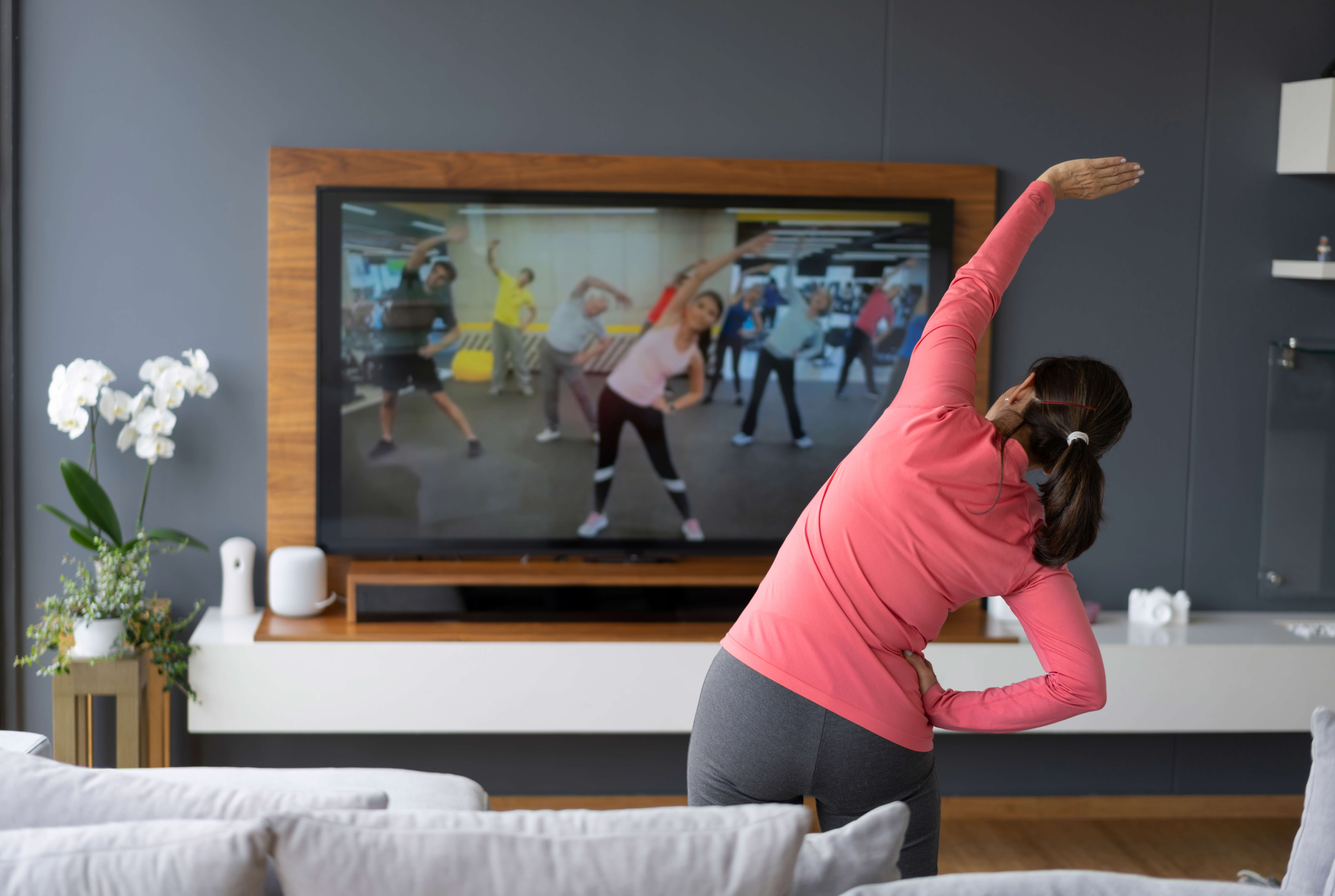 Main image: a woman in her living room, stretching her arm over her head doing an online fitness class to improve menopause symptoms.