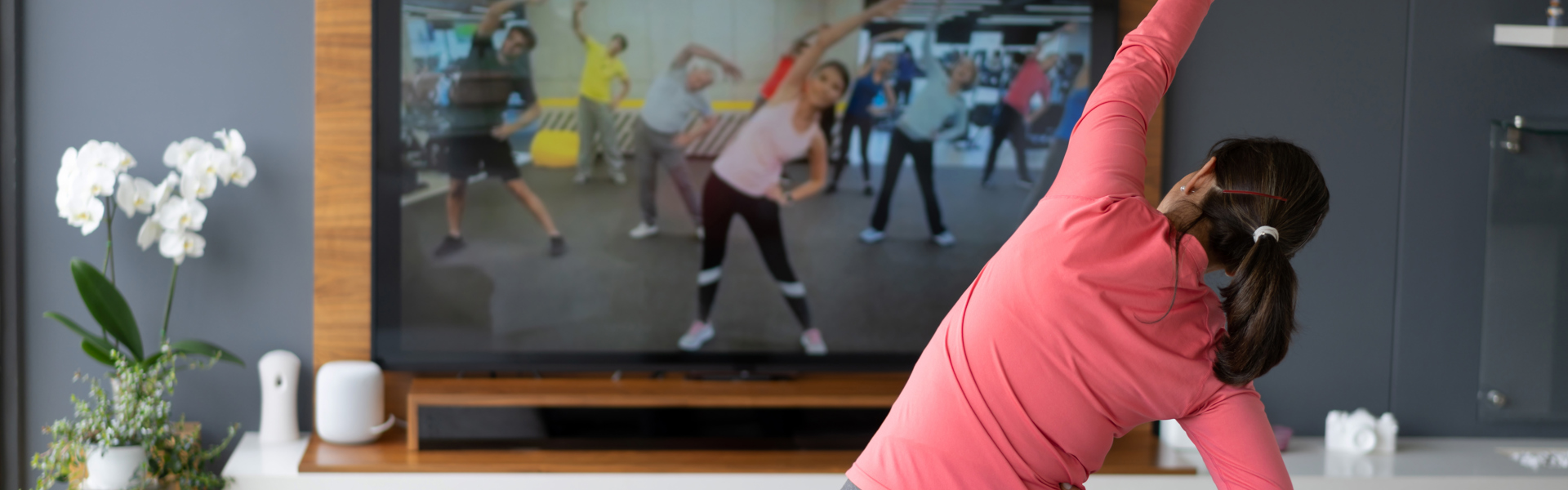 Main image: a woman in her living room, stretching her arm over her head doing an online fitness class to improve menopause symptoms.