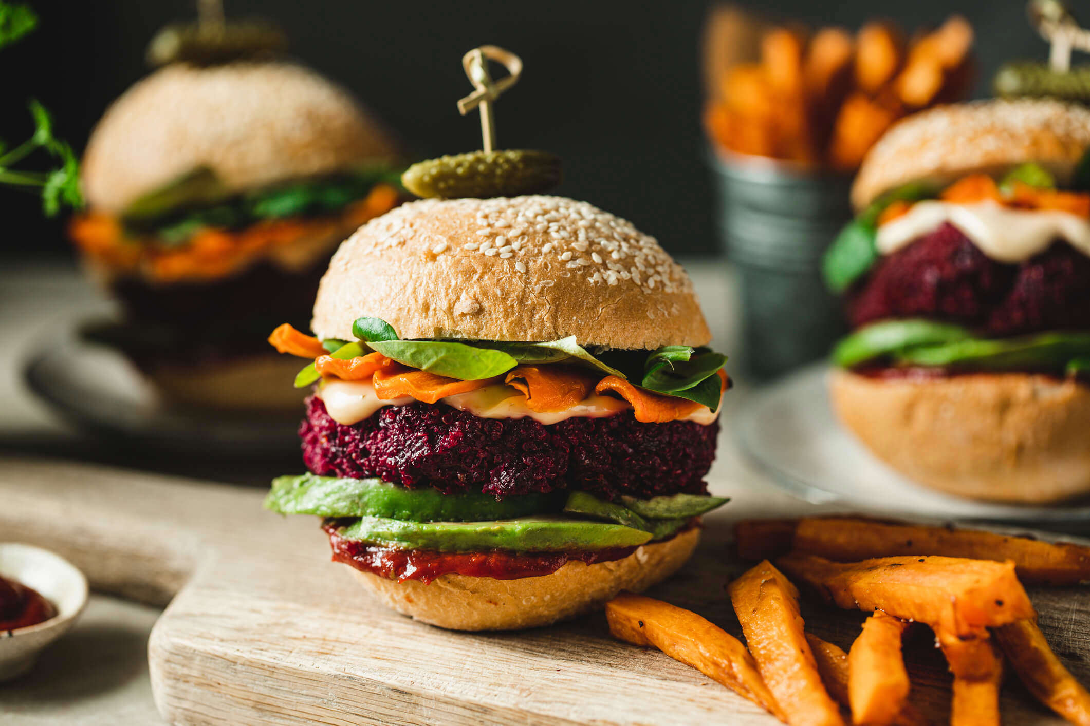 A beetroot burger with avocado and vegetables on a serving board with sweet potato fries