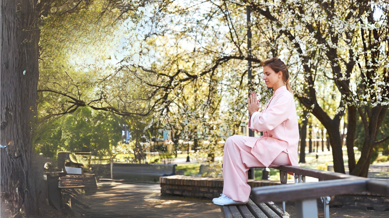 Main image: a woman sat on a bench in a park with her hand in a praying position, with trees all around her.