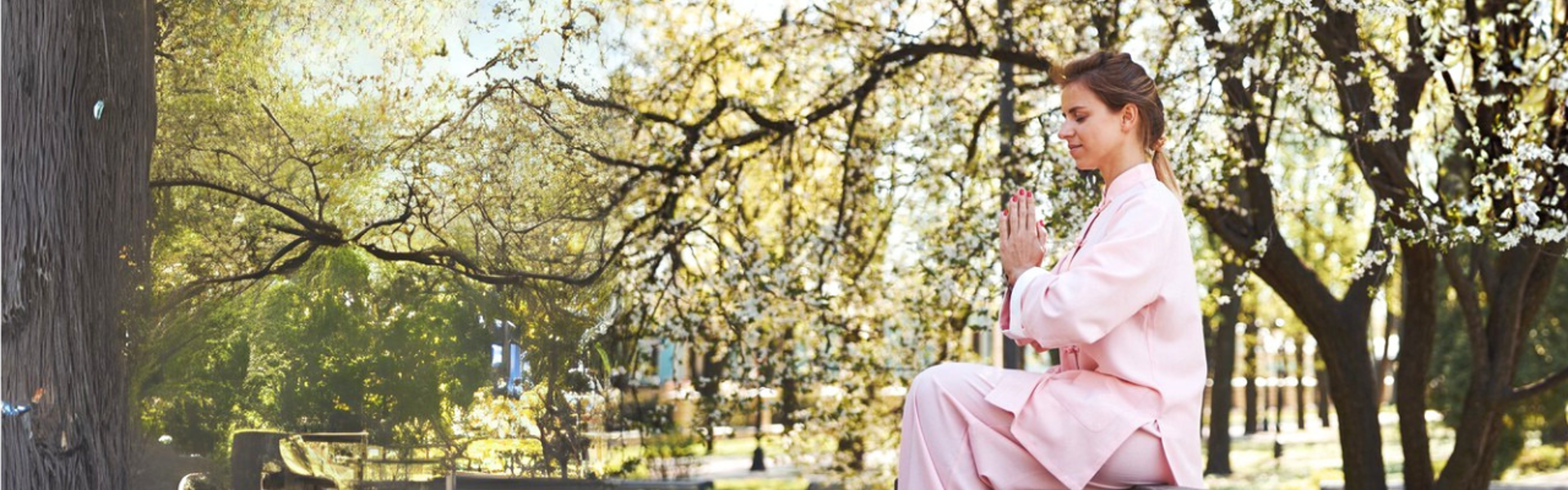 Main image: a woman sat on a bench in a park with her hand in a praying position, with trees all around her.