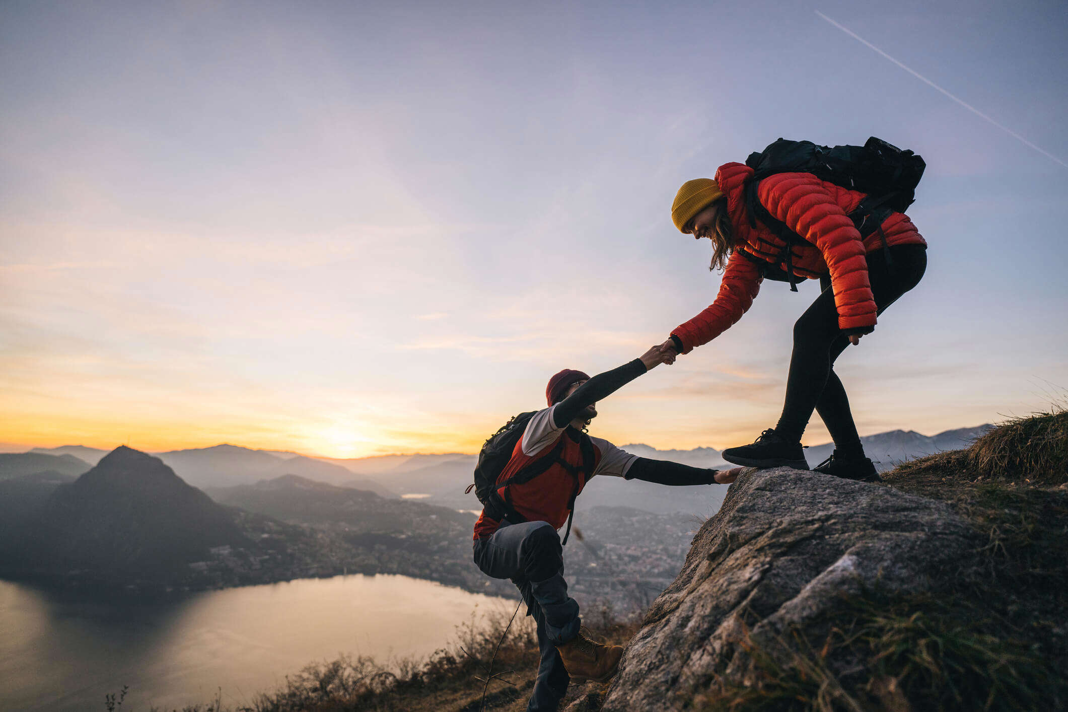 a person stood at the top of a mountain helping another person up to the summit